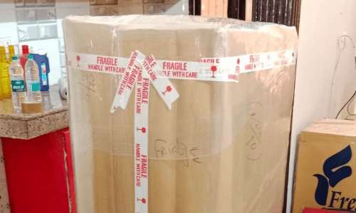 Best packers and movers wrapping a kitchen refrigerator with protective cardboard panels and clear stretch film